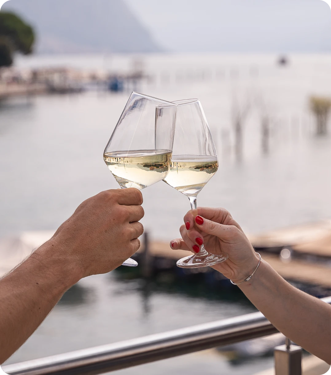 due mani che brindano con calici con vino bianco sul lungolago di Paratico