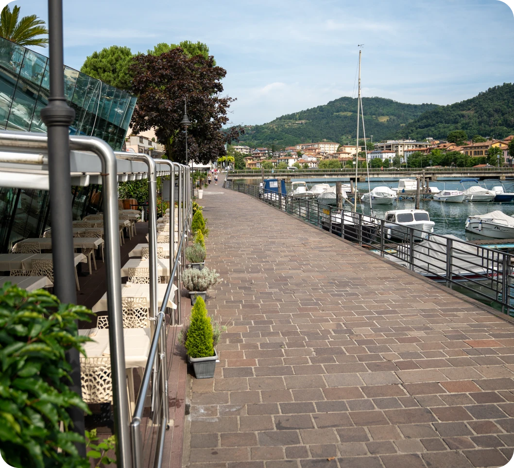 Lungolago di Paratico con tavoli esterni del ristorante Approdo a Paratico a sinistra e Lago d'Iseo con barche a destra